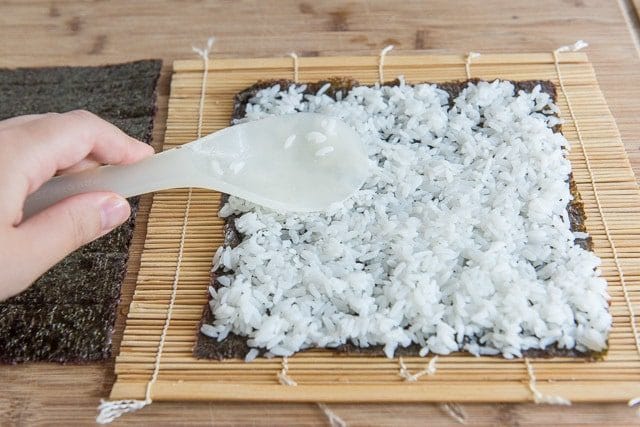 A piece of sushi seaweed with sushi rice spead on it.